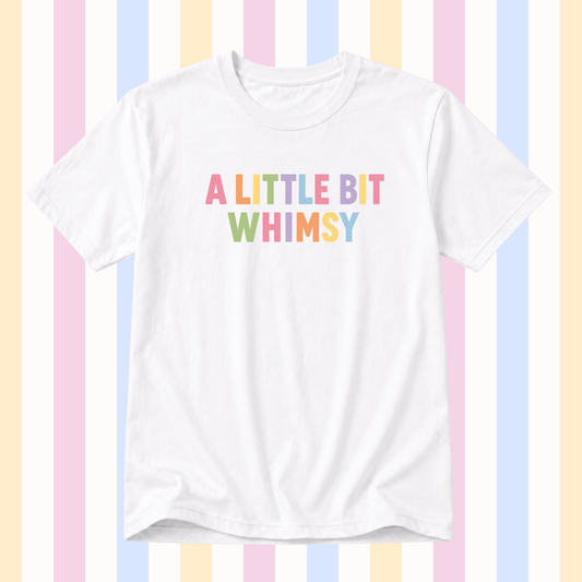 A white short-sleeve crewneck t-shirt featuring the text 'A LITTLE BIT WHIMSY' printed on the chest in a pastel rainbow font, set against a background of vertical pastel stripes.