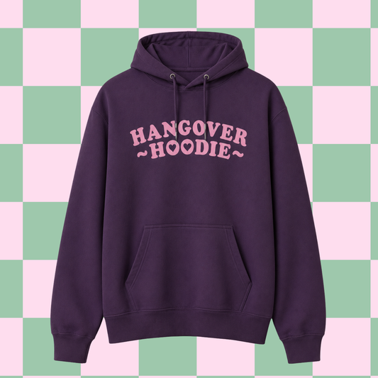 A dark purple pullover hoodie with 'HANGOVER HOODIE' printed in pink across the chest, displayed against a pastel pink and green checkered background.