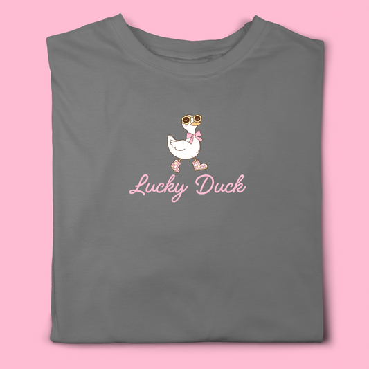 Grey t-shirt with cute duck illustration wearing sunglasses, bow, and pink boots, with slogan Lucky Duck in pink script.