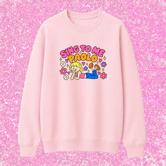 A light pink crewneck sweatshirt featuring a colorful graphic of a cartoon girl and the text 'SING TO ME PAOLO' in pink and yellow, displayed against a pink glitter background.