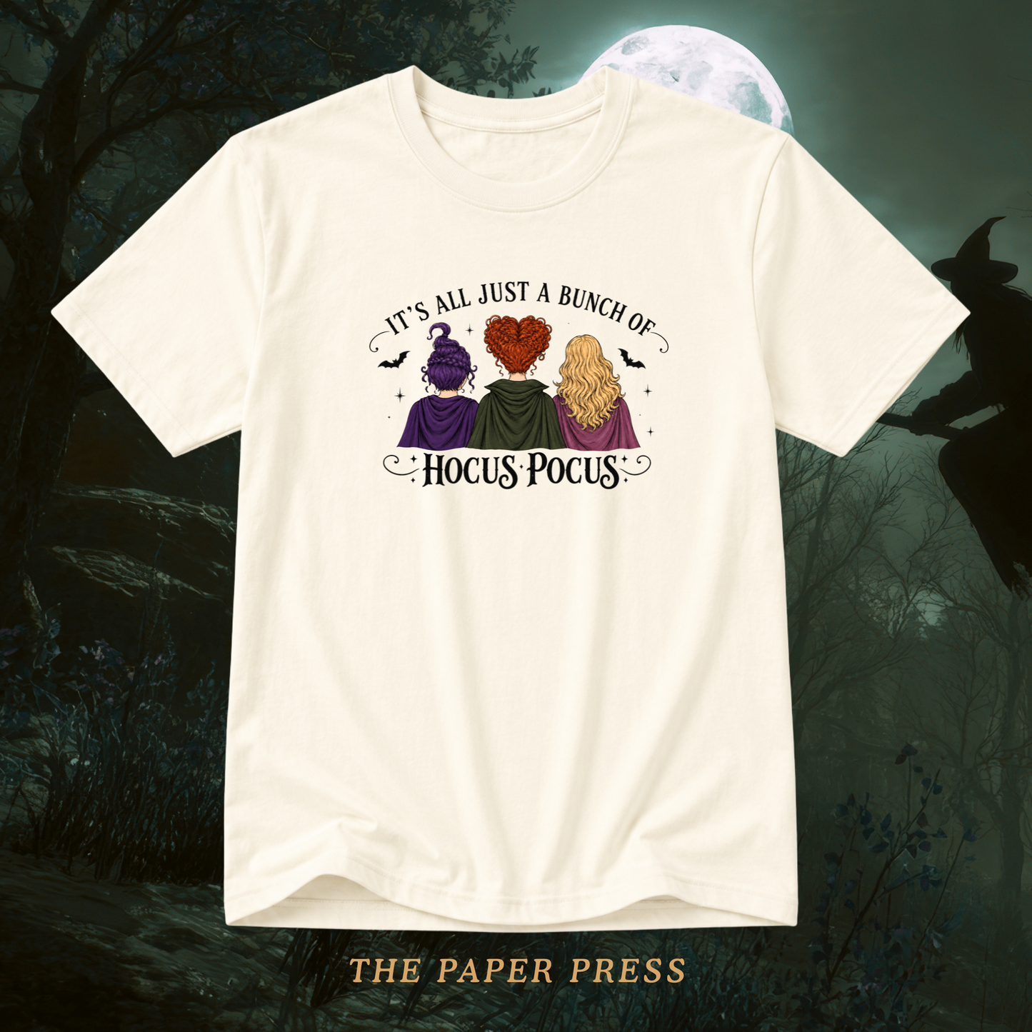 An off-white short-sleeve t-shirt with a Halloween-themed graphic print featuring three witches and the text 'It's All Just A Bunch Of Hocus Pocus'. The shirt is displayed against a dark, spooky background with a full moon and a witch silhouette, with 'THE PAPER PRESS' text at the bottom.