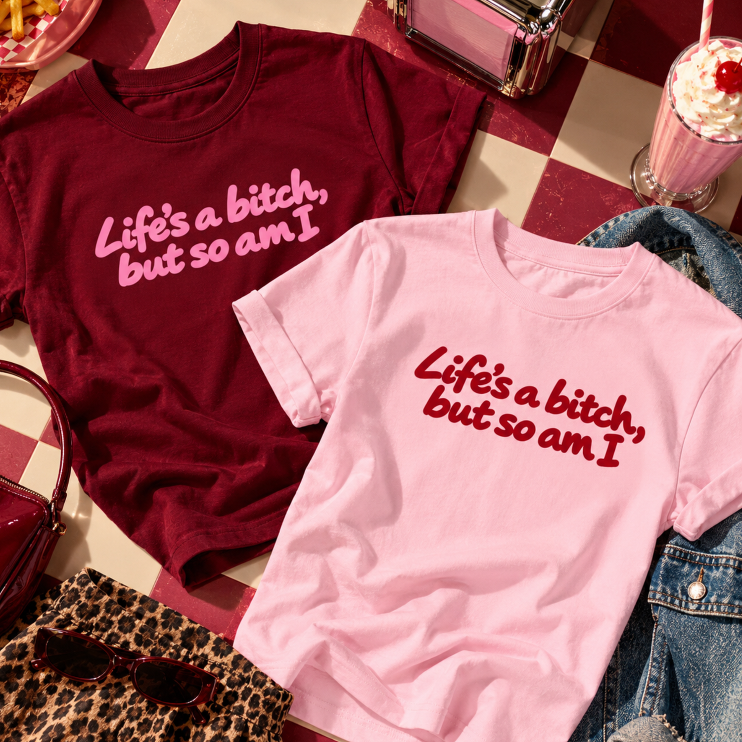 Life’s a Bitch But So Am I slogan T-shirts in baby pink with burgundy print and burgundy with pink print. Funny women’s graphic tees, hand-printed to order by The Paper Press in Northern Ireland. Styled on a retro diner-inspired checkerboard background.