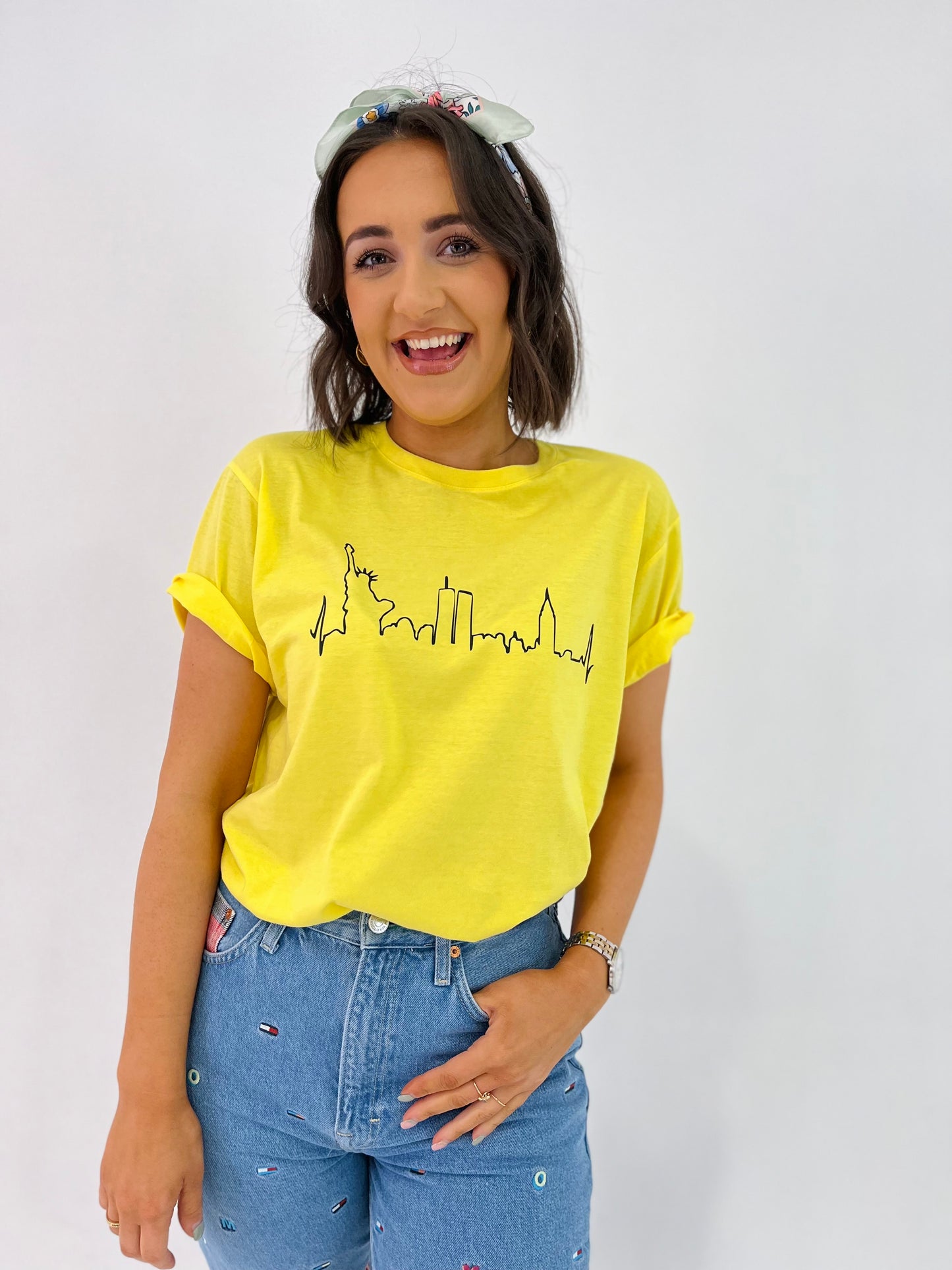 A person wearing a yellow crew neck t-shirt with 'New York' text and a skyline silhouette, paired with blue denim jeans.