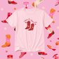 White t-shirt with cowboy boot design and text on a pink background with boot illustrations