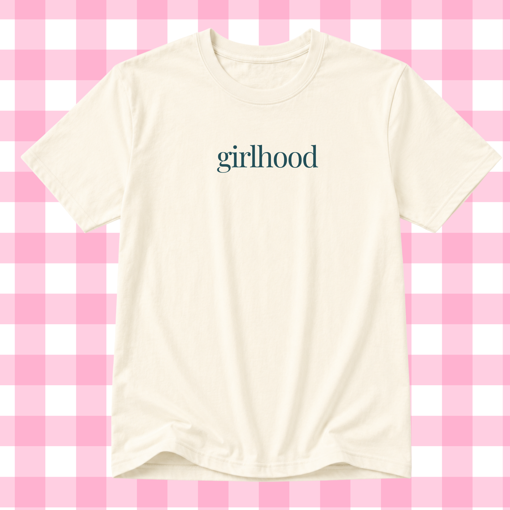 An off-white short-sleeve t-shirt with the word 'girlhood' printed in a dark teal serif font across the chest, displayed against a pink and white checkered background.