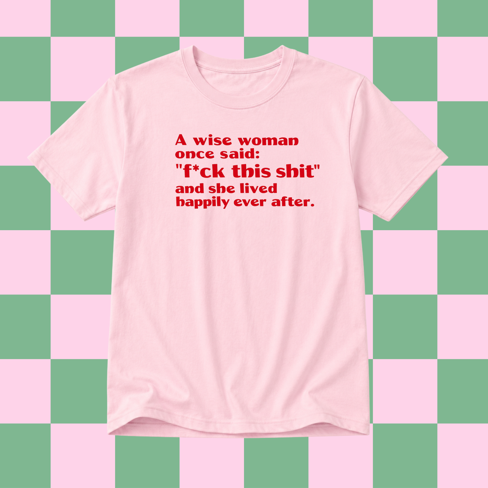 A light pink short-sleeve t-shirt with red printed text on the front, displayed against a pink and green checkered background.