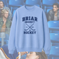 Light blue sweatshirt with 'Briar University Hockey' text and graphics on a blurred background of people.