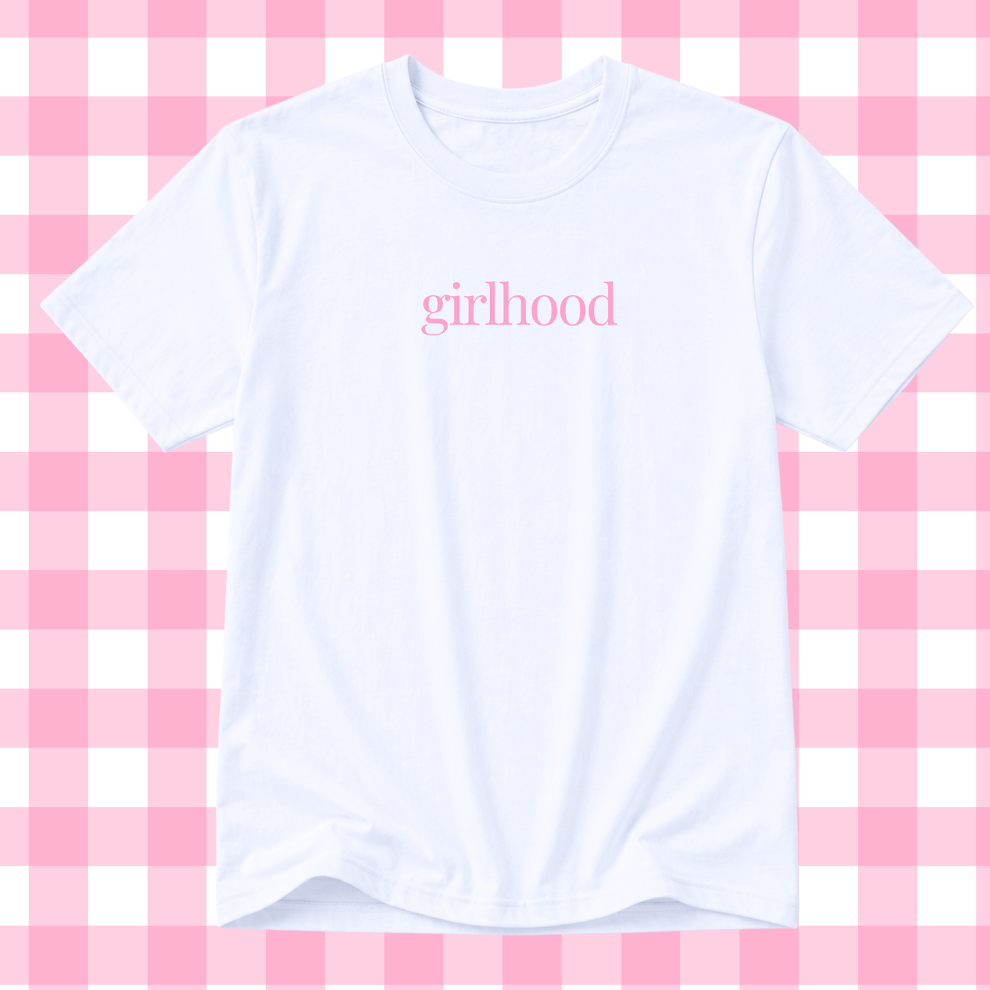 A white short-sleeve crewneck t-shirt with the word 'girlhood' printed in pink lowercase serif text across the chest, displayed against a pink and white checkered background.