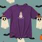 A purple short-sleeve t-shirt with a cute cartoon graphic of a ghost wearing a pink beanie and holding an autumn leaf, with the text 'I AM AN AUTUMN' below it. The t-shirt is displayed against a teal background decorated with Halloween-themed illustrations including ghosts, bats, and an orange pumpkin.