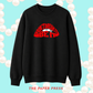 A black crewneck sweatshirt with a red graphic on the chest reading 'I DON'T DREAM IT BE IT' over white lips, displayed on a light blue background with white pearl-like circles and the text 'THE PAPER PRESS' at the bottom.