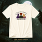 An off-white short-sleeve t-shirt with a Halloween-themed graphic print featuring three witches and the text 'It's All Just A Bunch Of Hocus Pocus'. The shirt is displayed against a dark, spooky background with a full moon and a witch silhouette, with 'THE PAPER PRESS' text at the bottom.